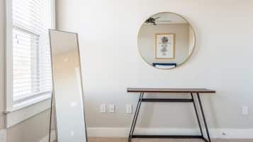 A room with a large mirror, a small table, and a window with blinds.