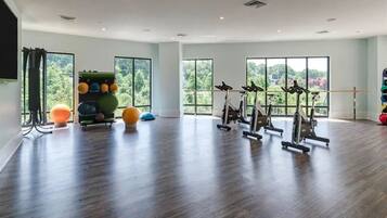A spacious gym with exercise bikes, a ball rack, and large windows offering a view of greenery.