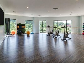 A spacious gym with exercise bikes, a ball rack, and large windows offering a view of greenery.