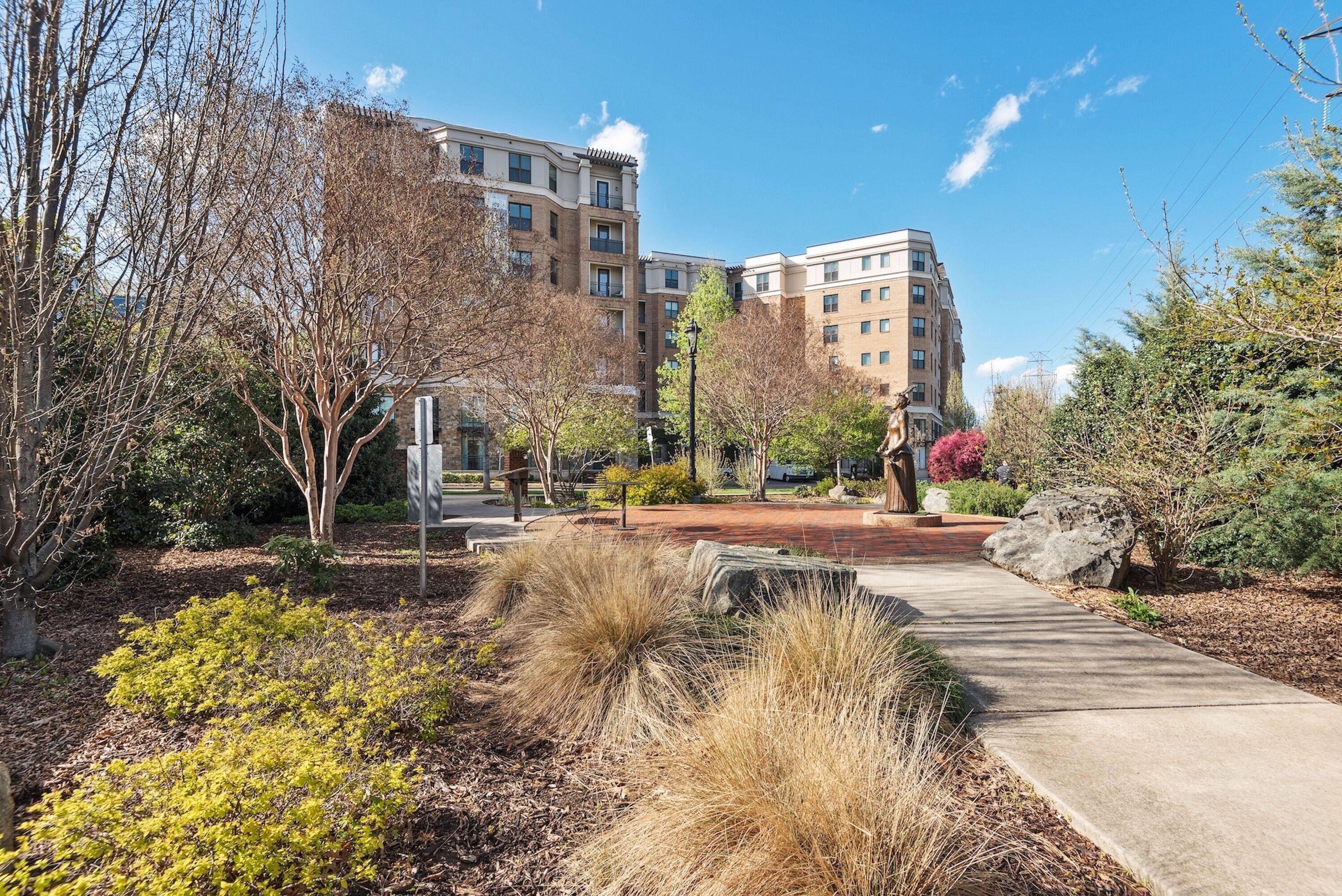 A landscaped courtyard with a pathway, trees, and a multi-story building in the background.