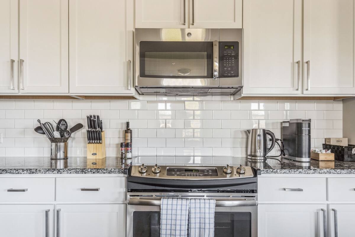 A kitchen with white cabinets, a stainless steel microwave, a gas stove, and a kettle.