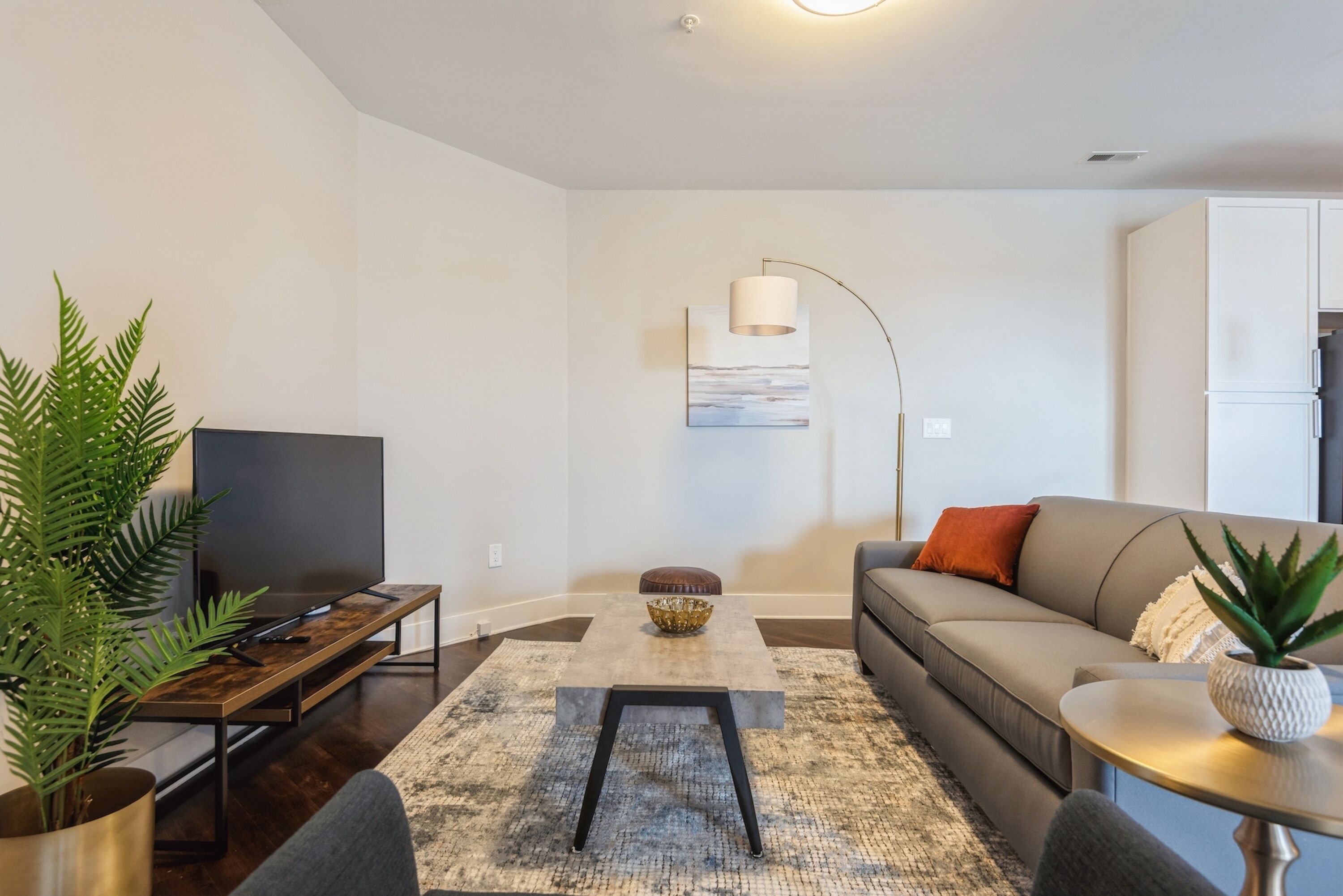Una sala de estar moderna con una televisión de pantalla plana, un sofá, una mesa de centro y una lámpara de pie.