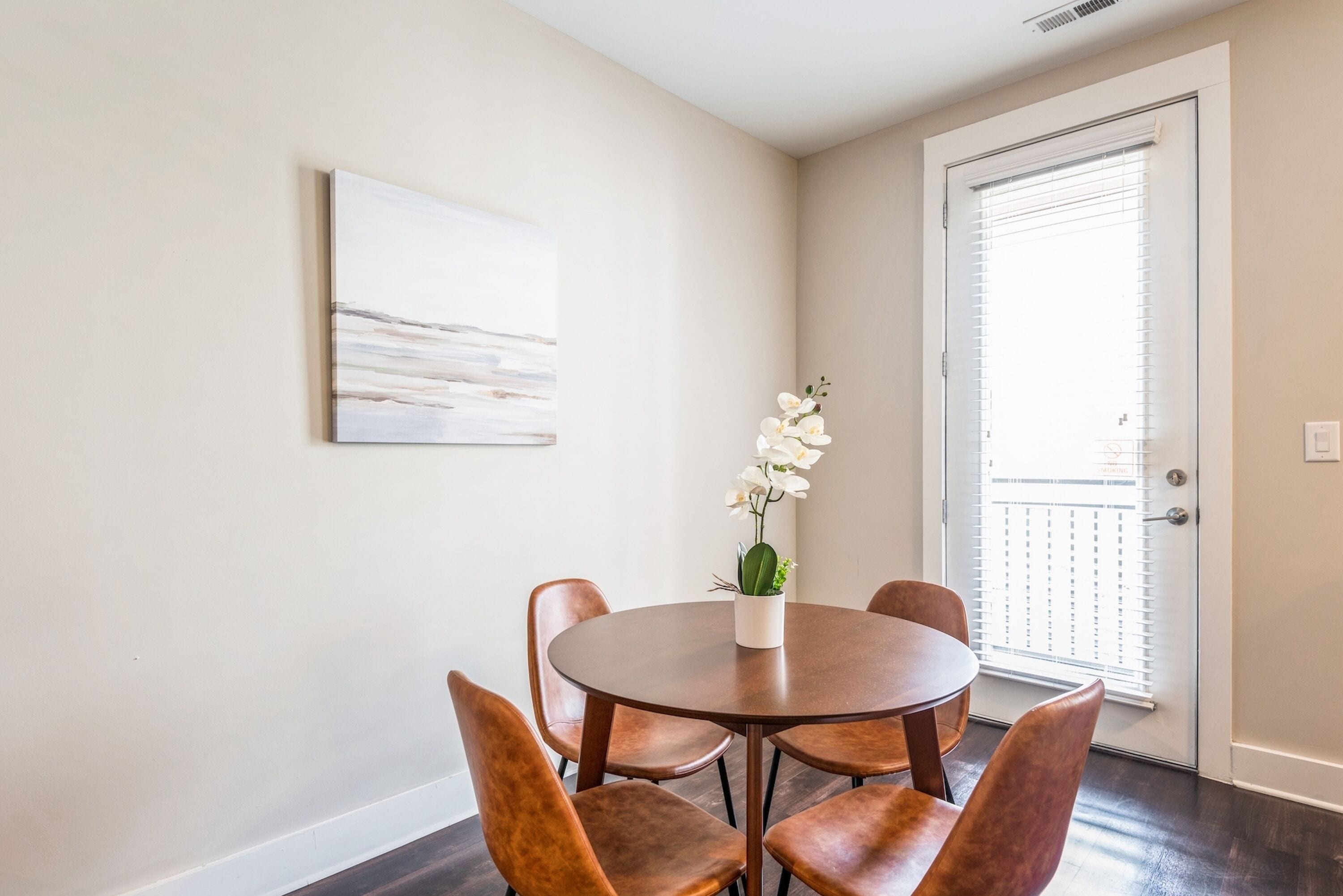 A dining area with a round table, six chairs, and a vase with white flowers.