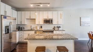 A modern kitchen with white cabinets, granite countertops, stainless steel appliances, and pendant lighting. - Kasa Dilworth Charlotte (Charlotte)