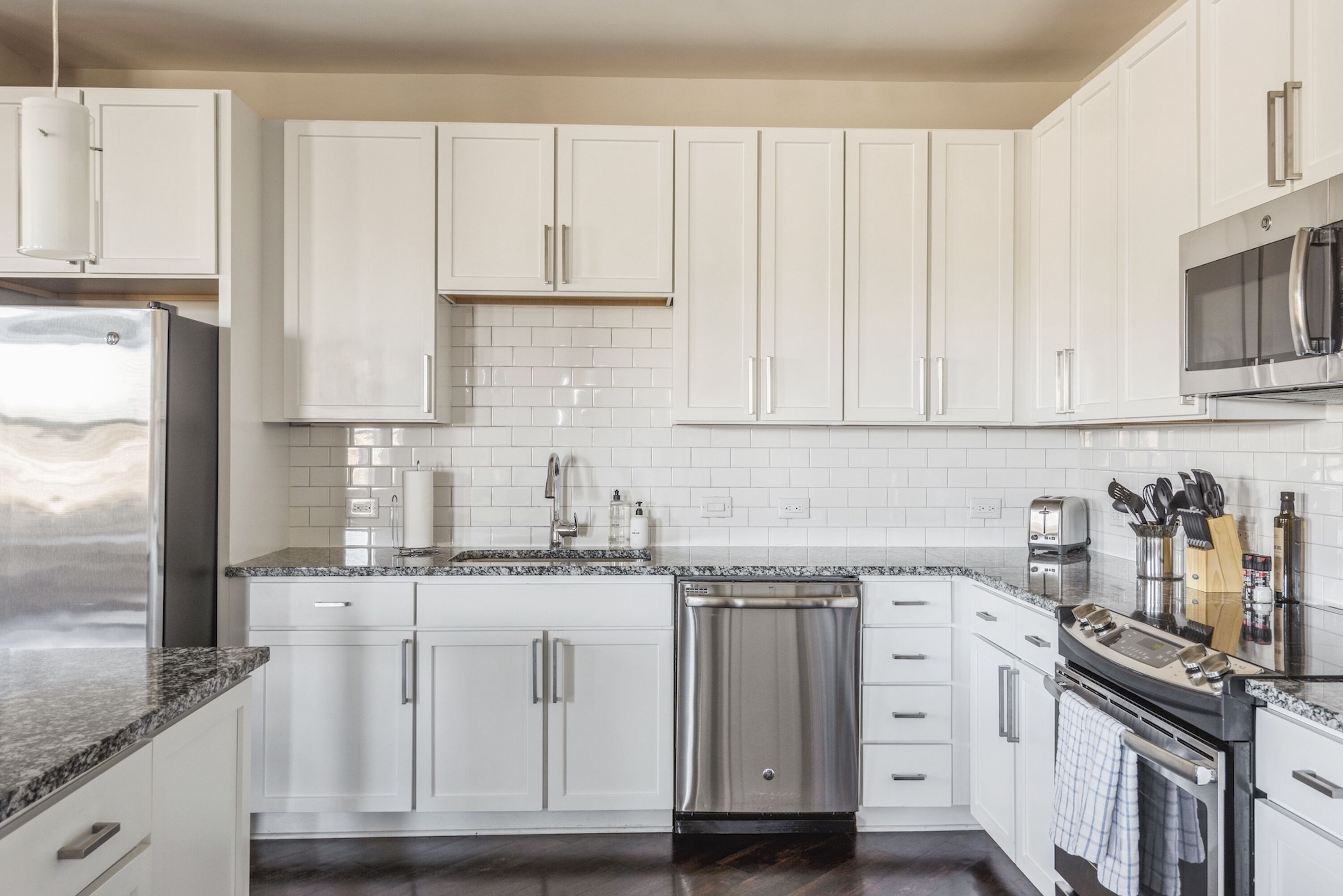 A modern kitchen with white cabinets, a stainless steel refrigerator, a dishwasher, and a microwave.