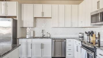 A modern kitchen with white cabinets, a stainless steel refrigerator, a dishwasher, and a microwave.