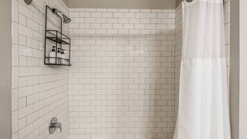A shower area with white tiled walls, a chrome showerhead, a glass shower caddy, and a white shower curtain.