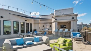 An outdoor patio area with seating arrangements, a barbecue grill, and string lights. - Kasa Dilworth Charlotte (Charlotte)