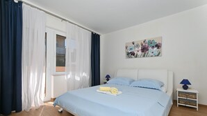 A bedroom with a bed, a window with curtains, a painting, and a bedside table. - Radelic, comfortable two bedroom apartment (Mastrinka)