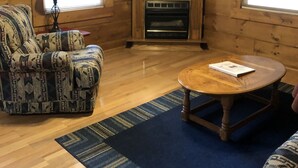 Un salon chaleureux avec un canapé à motifs, une table basse ronde en bois, une cheminée et un téléviseur fixé au-dessus.