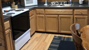 Une cuisine compacte avec des meubles en bois, un four à micro-ondes, une cuisinière, un évier et une fenêtre avec des stores.