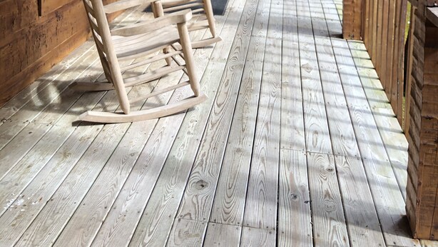 Une terrasse en bois avec plusieurs fauteuils à bascule, une rambarde en bois et une vue sur la forêt.
