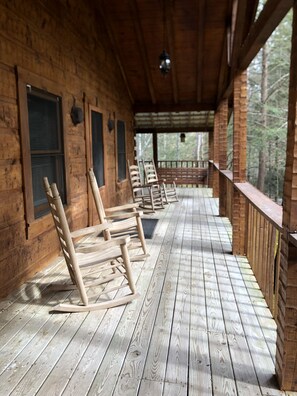 Une terrasse en bois avec plusieurs fauteuils à bascule, une rambarde en bois et une vue sur la forêt.