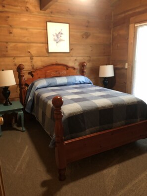 Une chambre à coucher aux murs lambrissés, avec un lit, deux tables de chevet et une petite table d’appoint.