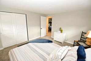 Une chambre avec deux lits, une commode, une chaise et une lampe.