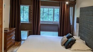 A bedroom with a large bed, wooden ceiling beams, a dresser, and a window with curtains.