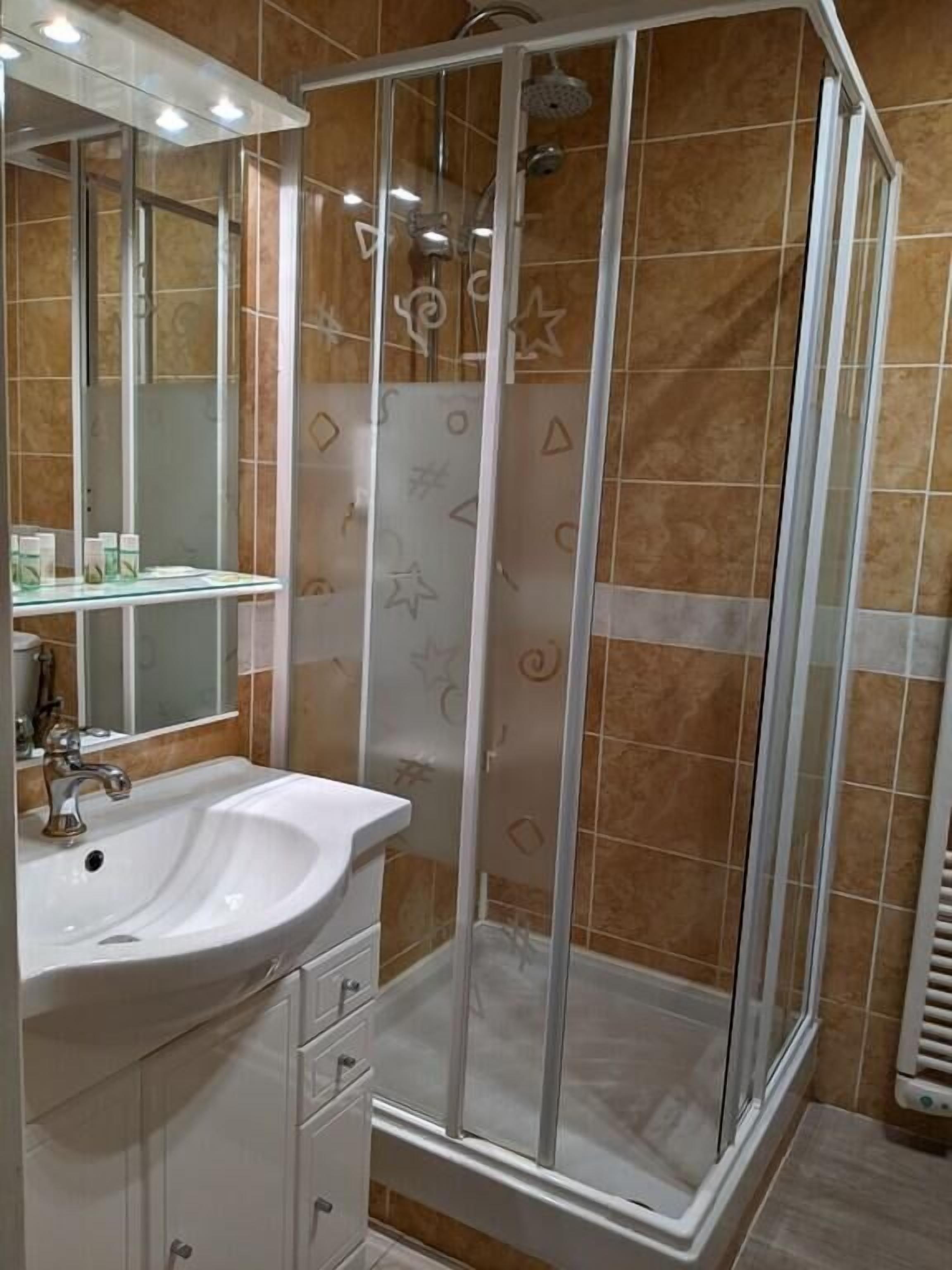 A bathroom with a white sink, a mirror, a shower enclosure, and tiled walls.