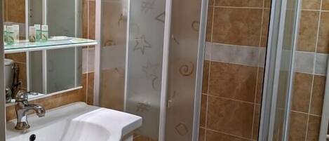 A bathroom with a white sink, a mirror, a shower enclosure, and tiled walls.