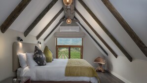 A bedroom with a large bed, wooden beams, a window with a view, and a bedside lamp.