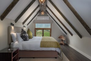 A bedroom with a large bed, wooden beams, a window with a view, and a bedside lamp.