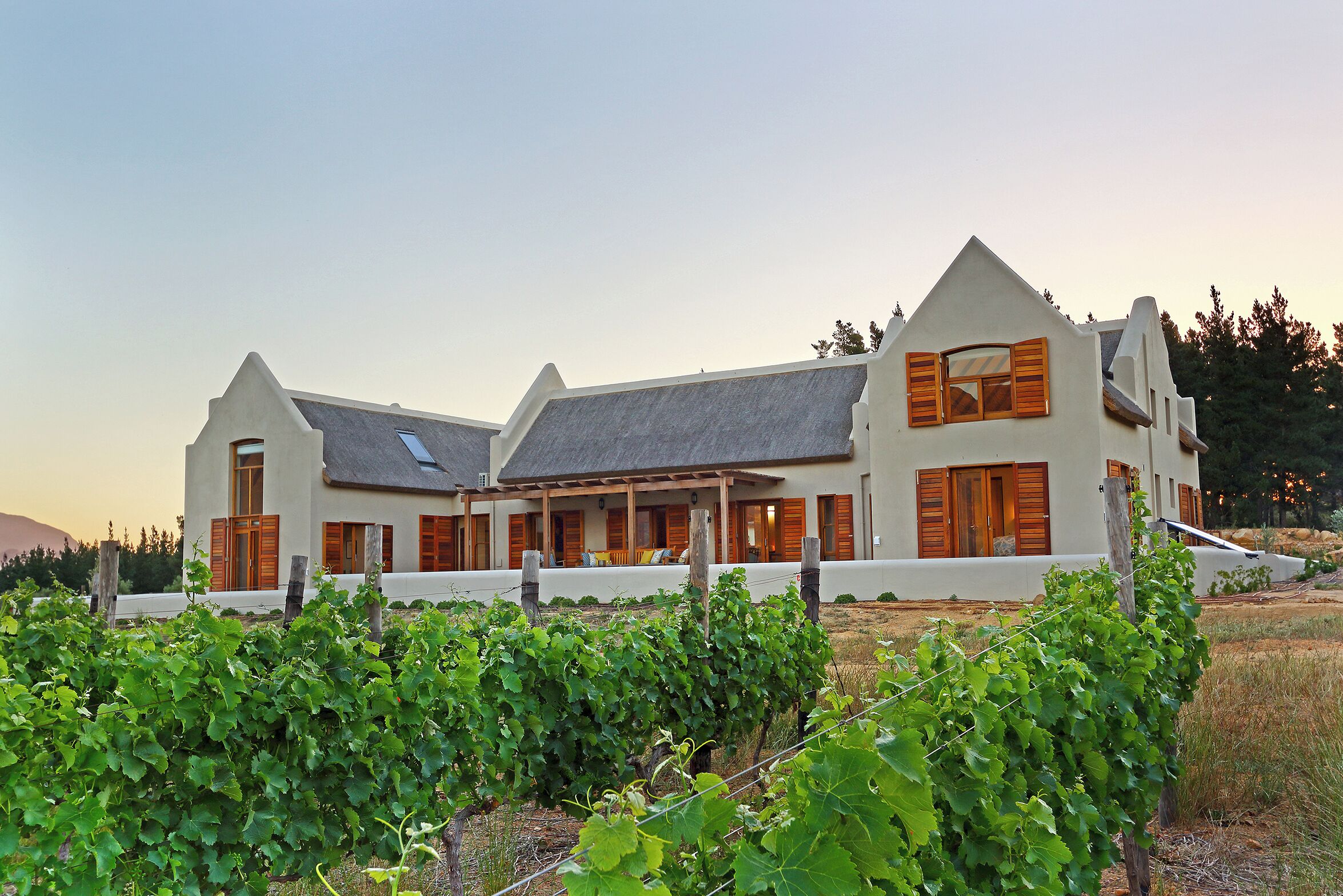A large, white building with a sloped roof and wooden shutters, surrounded by a vineyard.