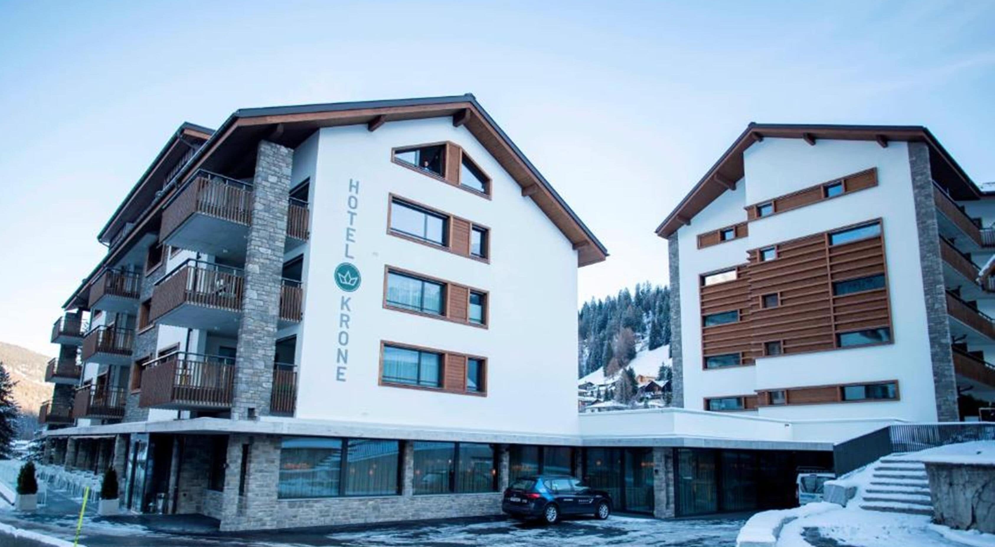 Un hotel moderno con fachada blanca, varios balcones y un área de estacionamiento.
