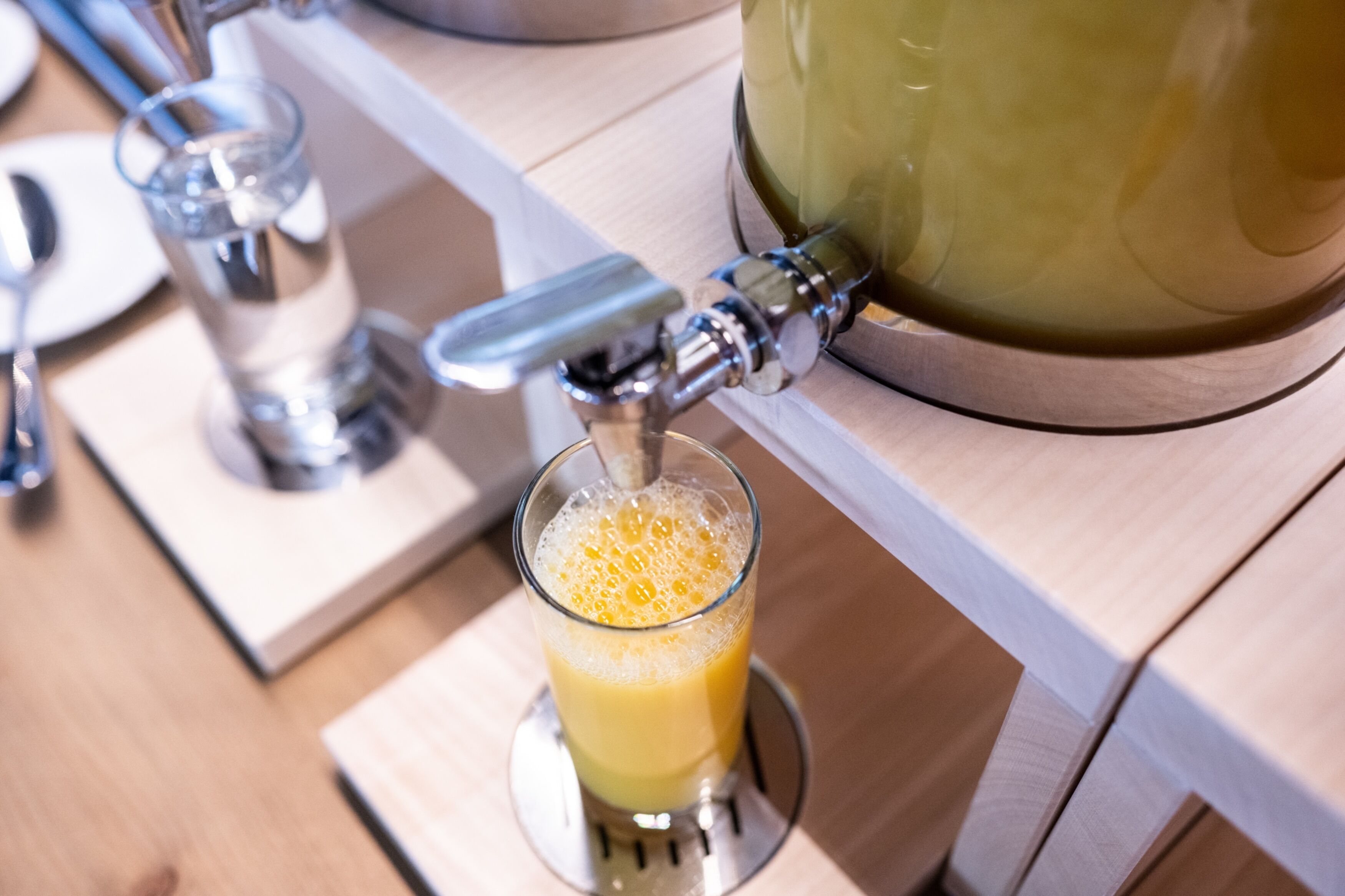 A juice dispenser with a glass of orange juice being filled.