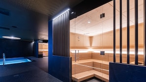 Un espace spa moderne doté d’un plancher chauffant, de bancs en bois et de cloisons en verre.