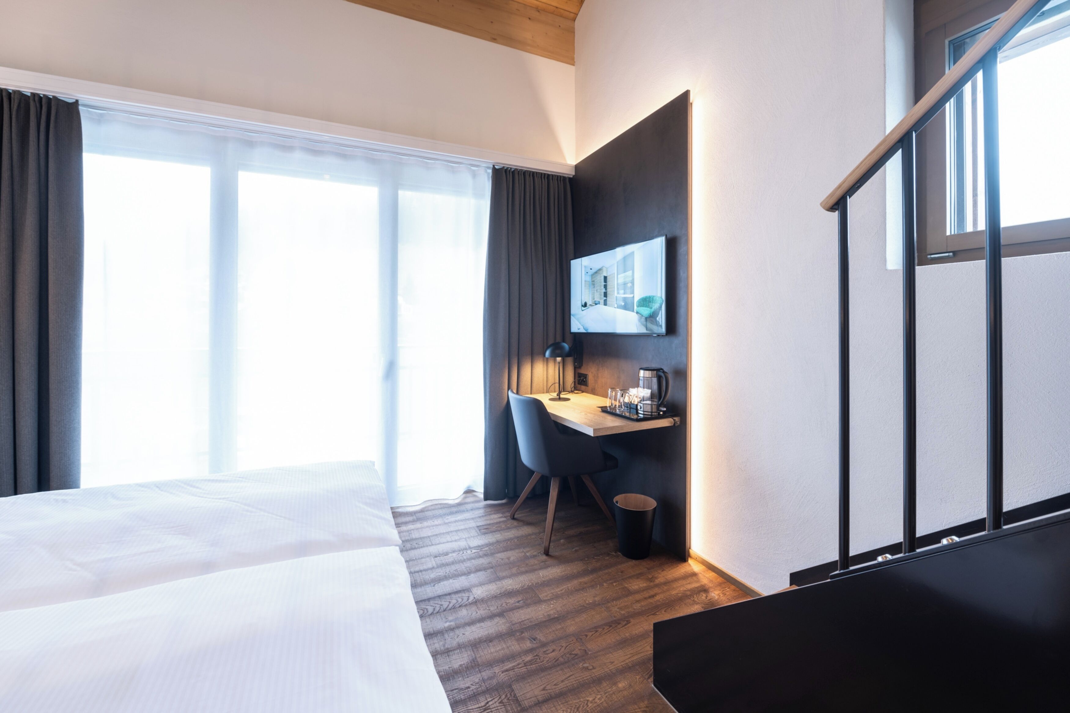 Une chambre d’hôtel avec un grand lit, un bureau avec une chaise, un téléviseur fixé au mur et une fenêtre avec des rideaux.