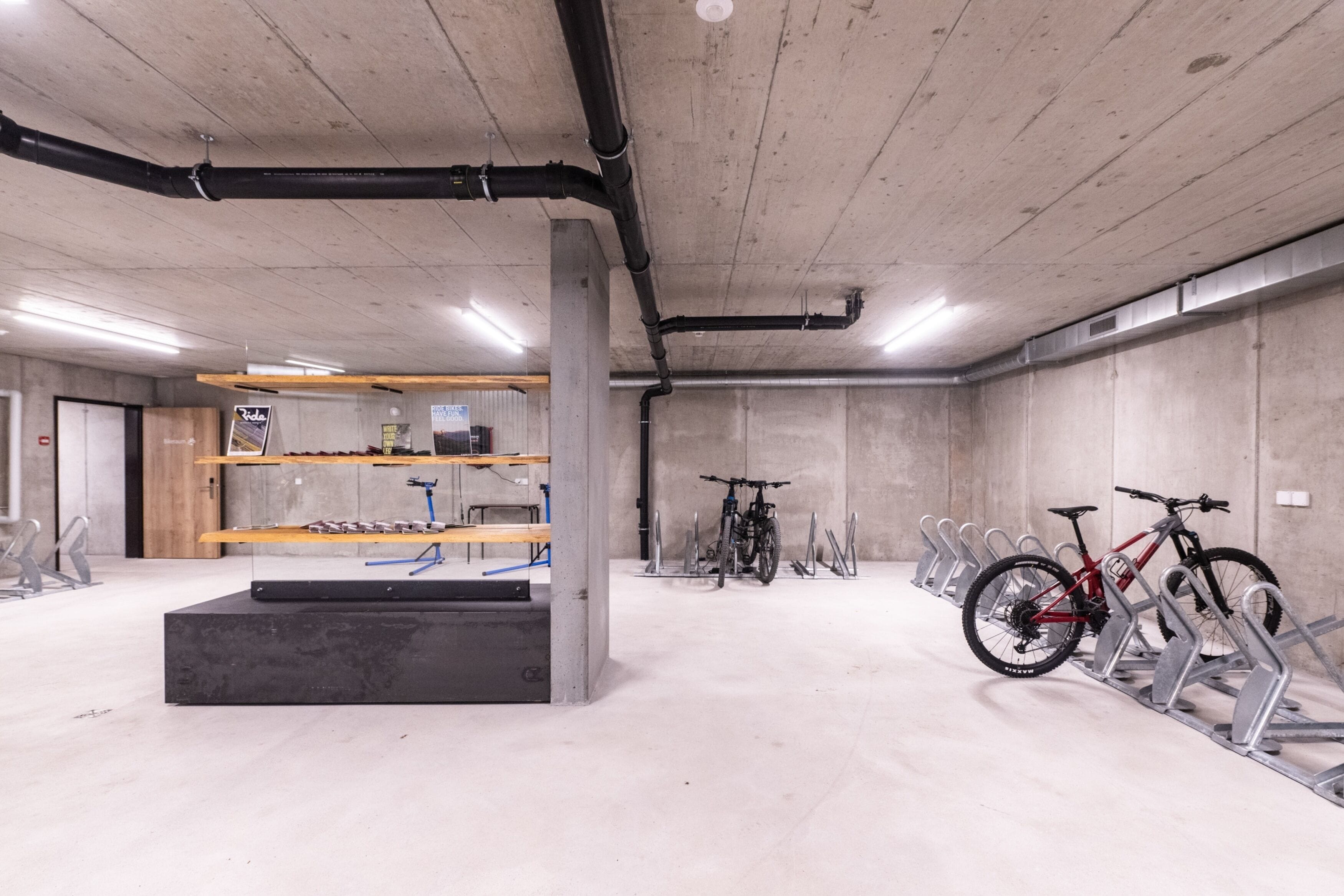 A bike parking area with multiple racks, a wooden shelf unit, and a concrete floor.