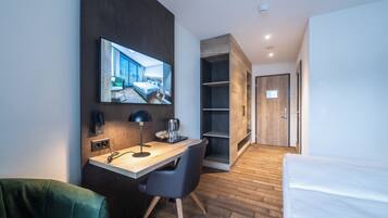 Una habitación de hotel moderna con un escritorio de madera, una cama, un televisor montado en la pared y un armario.