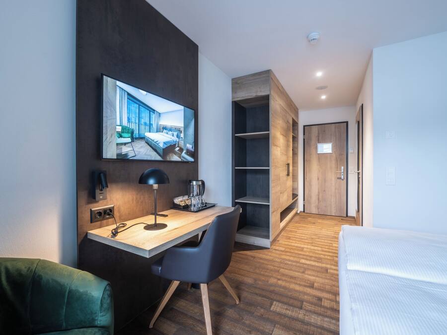 Una habitación de hotel moderna con un escritorio de madera, una cama, un televisor montado en la pared y un armario.