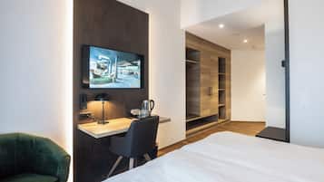 Una habitación de hotel moderna con una cama, un escritorio con silla, un televisor en la pared y un armario.