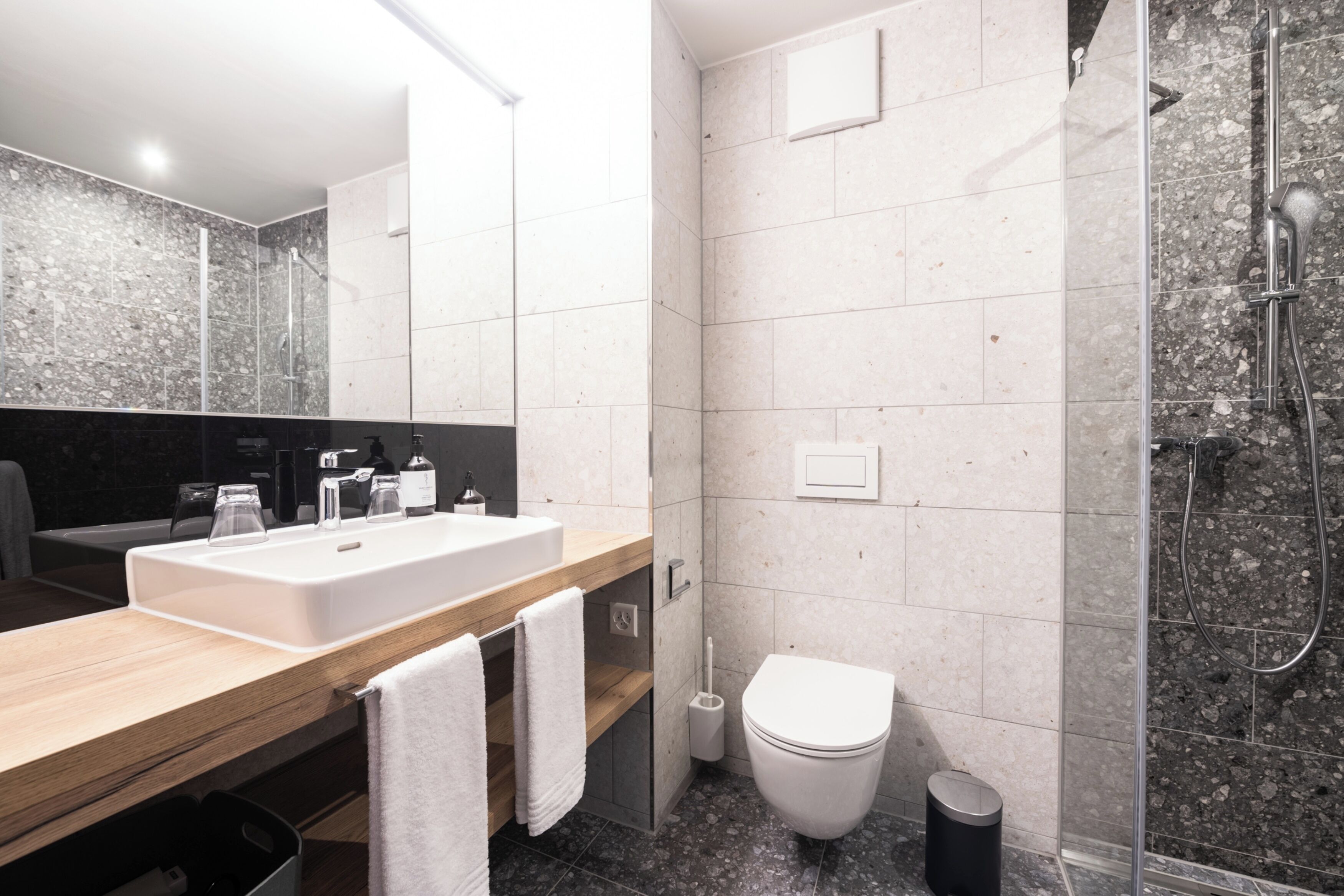Une salle de bain moderne avec un meuble-lavabo en bois, un lavabo blanc et une cabine de douche en verre.