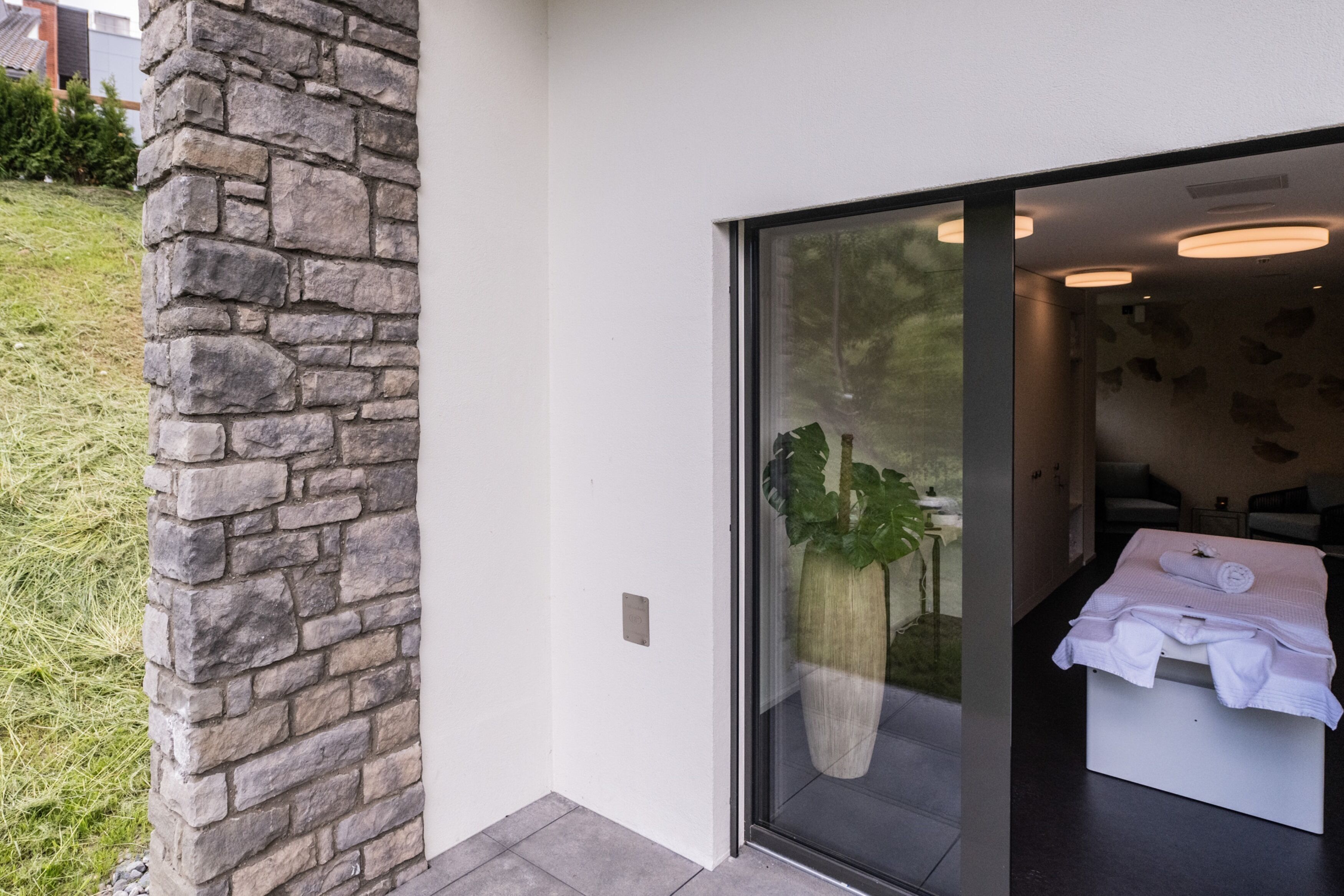 A modern bathroom with a large window, a stone wall, and a potted plant.