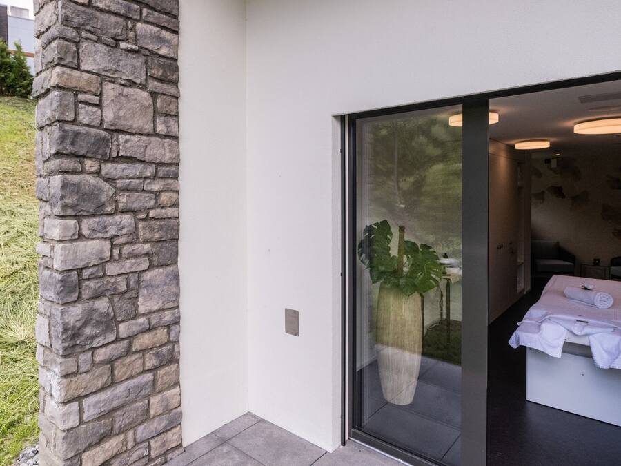 A modern bathroom with a large window, a stone wall, and a potted plant.