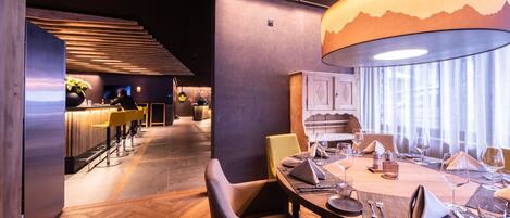 A modern restaurant with a wooden floor, a dining area with tables set for two, and a bar area with stools.