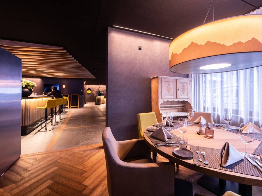A modern restaurant with a wooden floor, a dining area with tables set for two, and a bar area with stools.