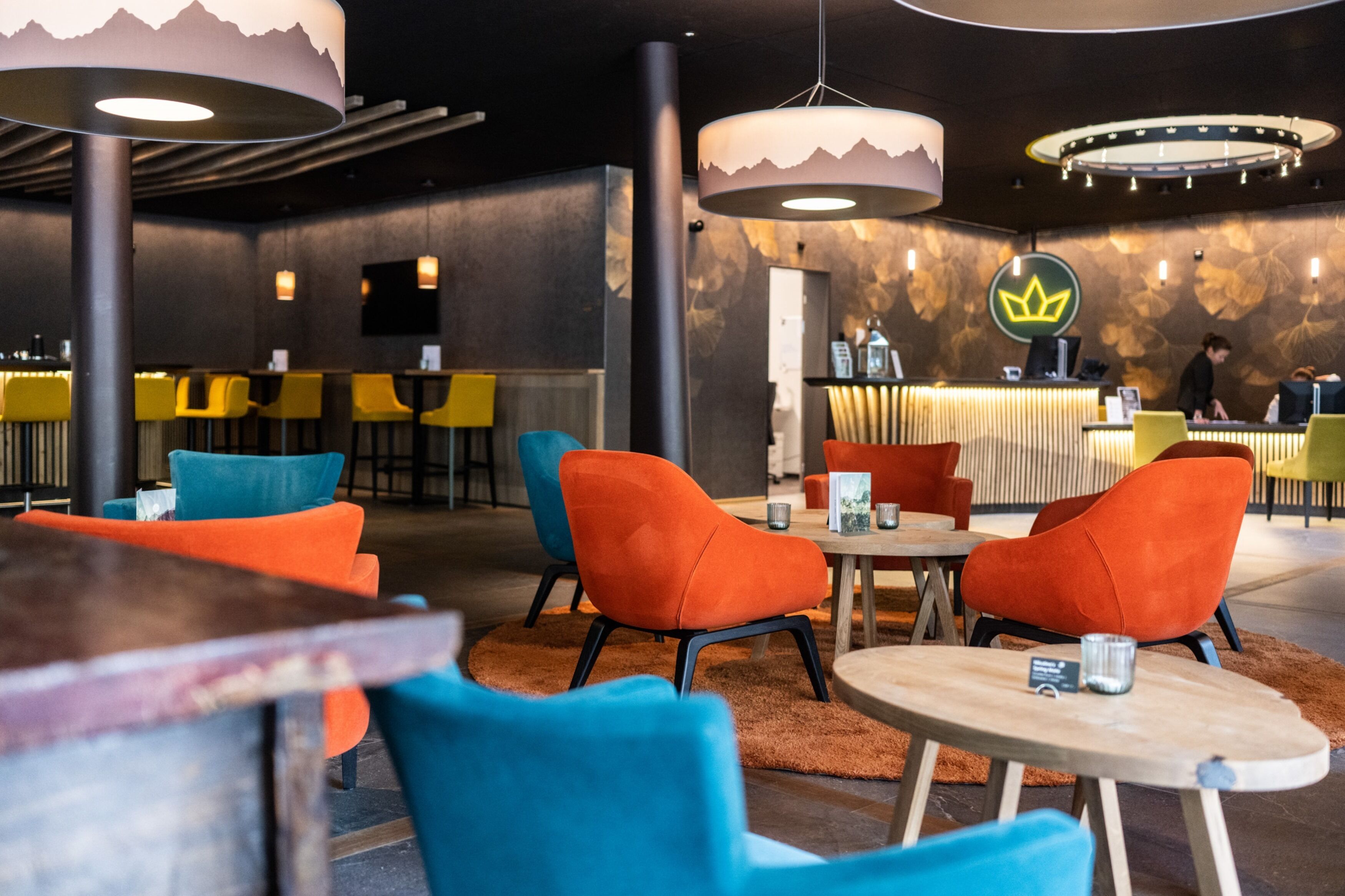 Un interior modern amb cadires taronja i blaves, taules de fusta i una zona de bar amb barra.