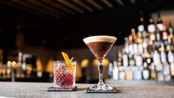 Two cocktails on coasters at a bar with a blurred background of bottles.