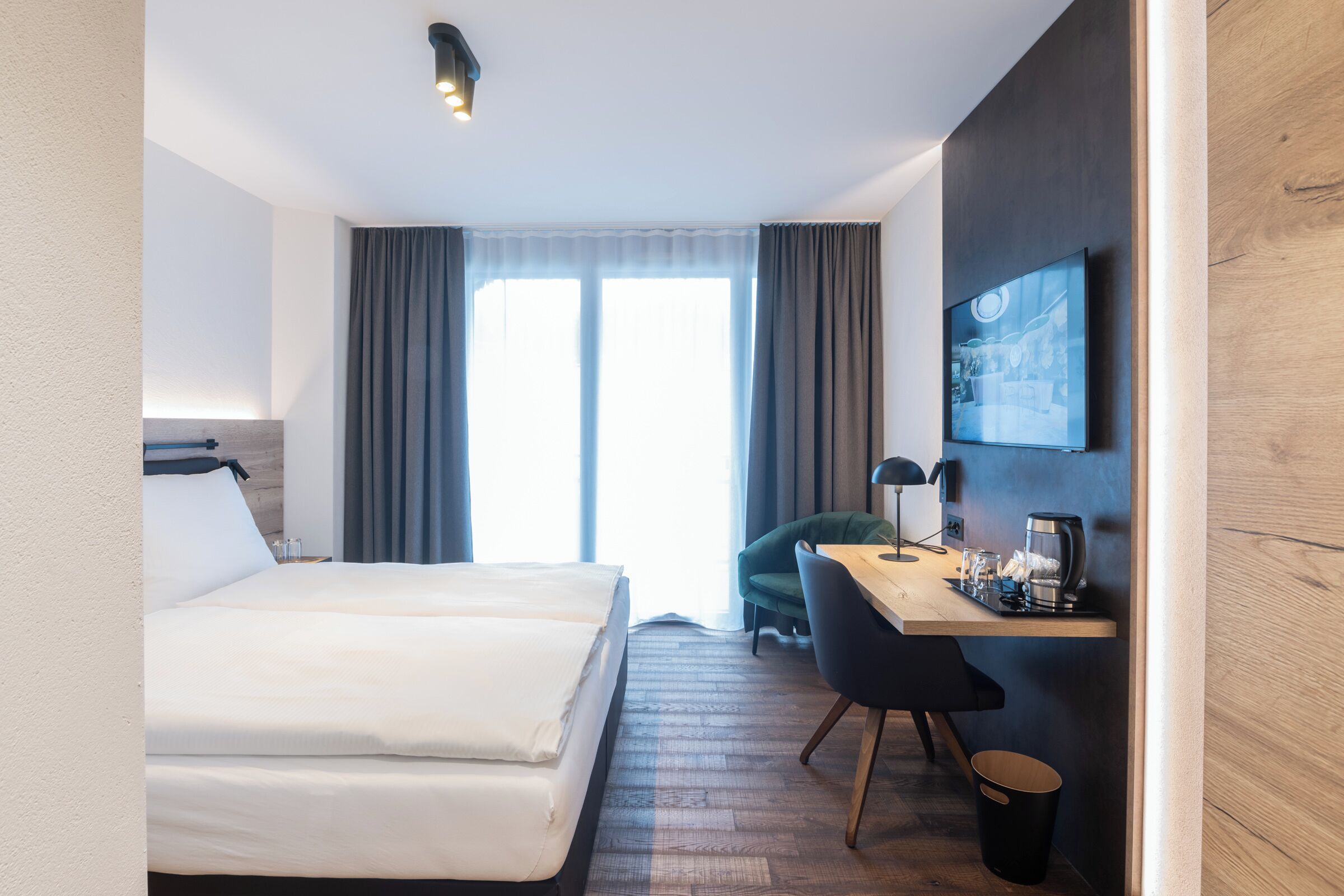 A hotel room with a bed, a desk, a chair, a television, and a window with curtains.