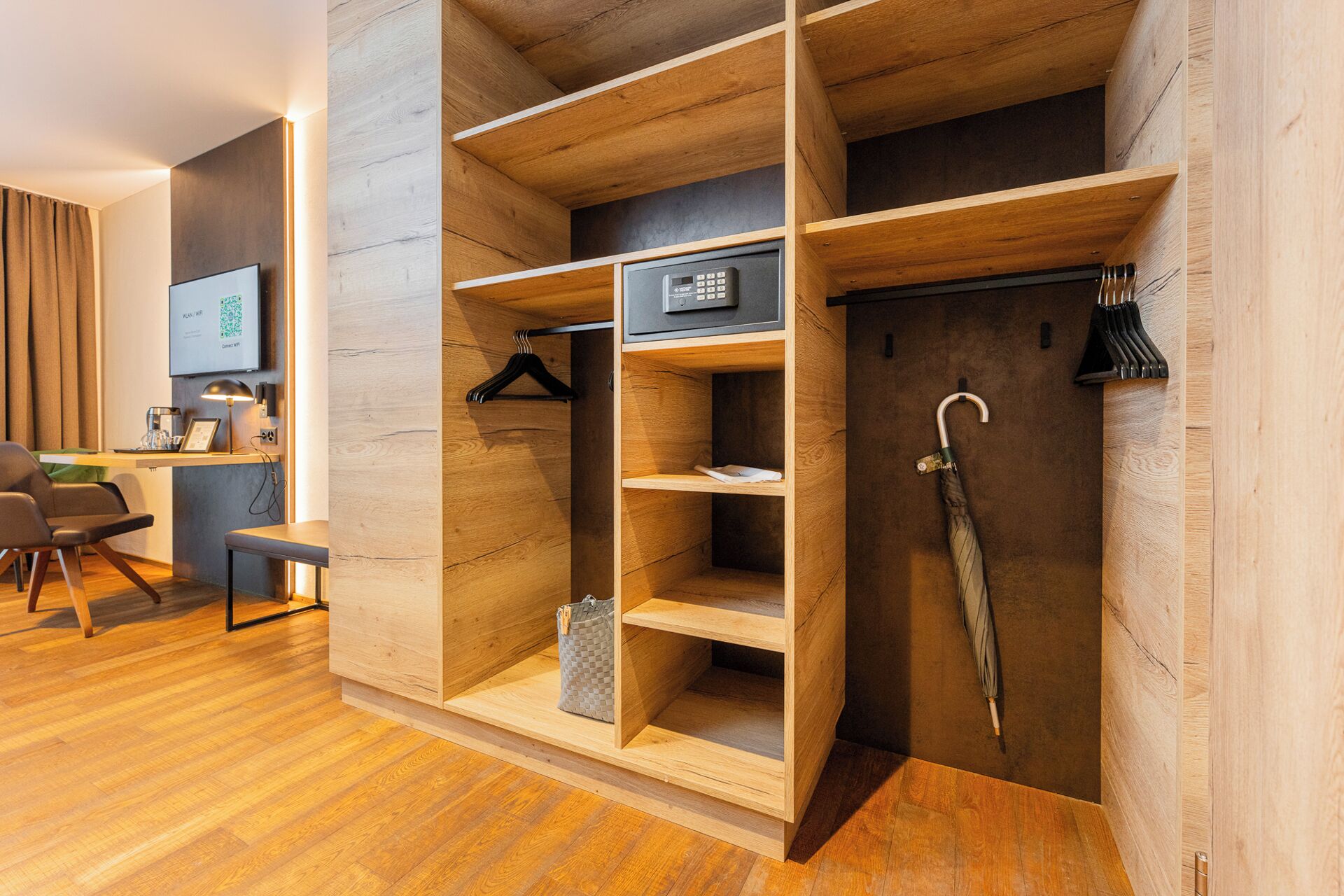 A modern hotel room with a wooden wardrobe, a desk with a chair, and a coat rack.