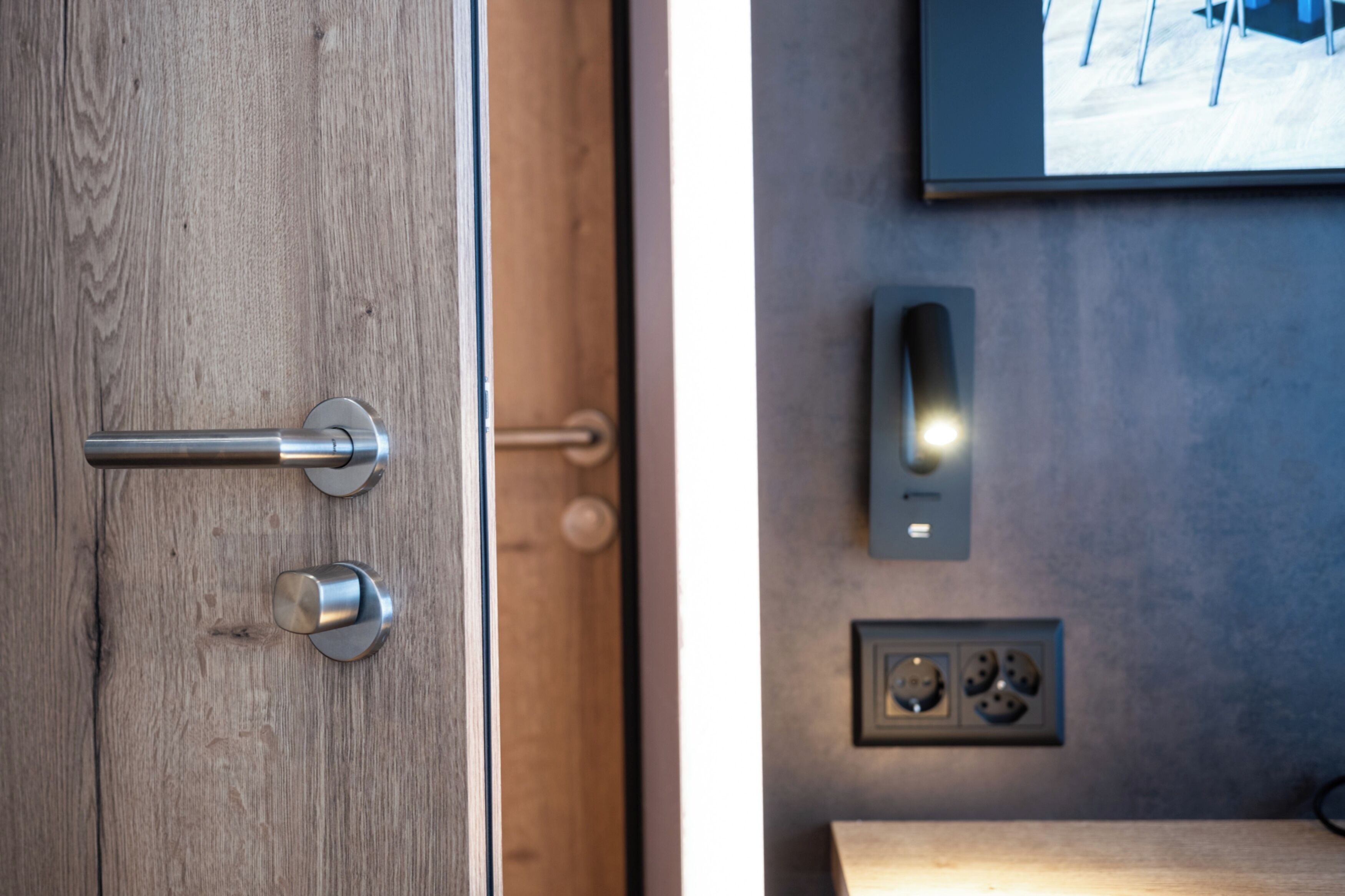 Una puerta de madera con un picaporte moderno e interruptor de luz adosado a la pared.