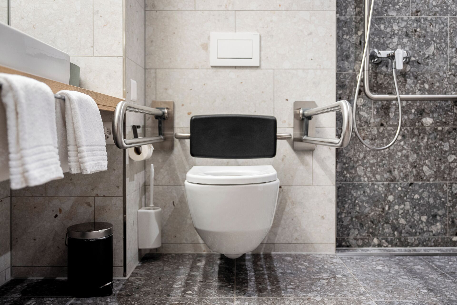 Ein modernes Badezimmer mit Toilette, Haltegriffen, einem Mülleimer und einer Duschkabine.