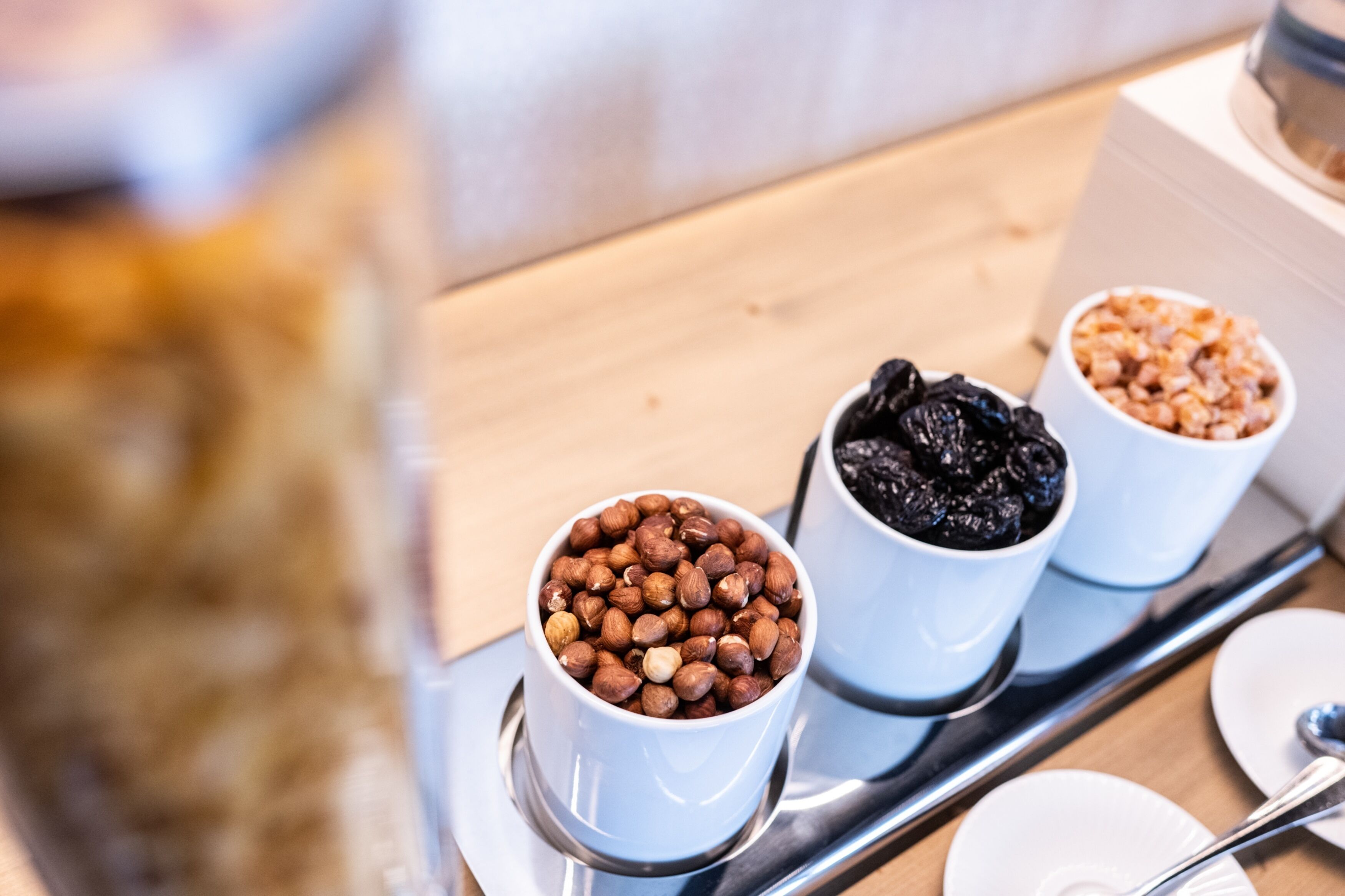 Three white cups on a tray, each containing different items: nuts, dried fruits, and a mix of nuts and dried fruits.
