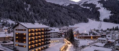 A modern hotel with multiple floors, a ski slope in the background, and a snowy landscape.