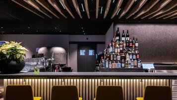 A bar area with a wooden ceiling, a bar counter with multiple bottles, and yellow chairs.