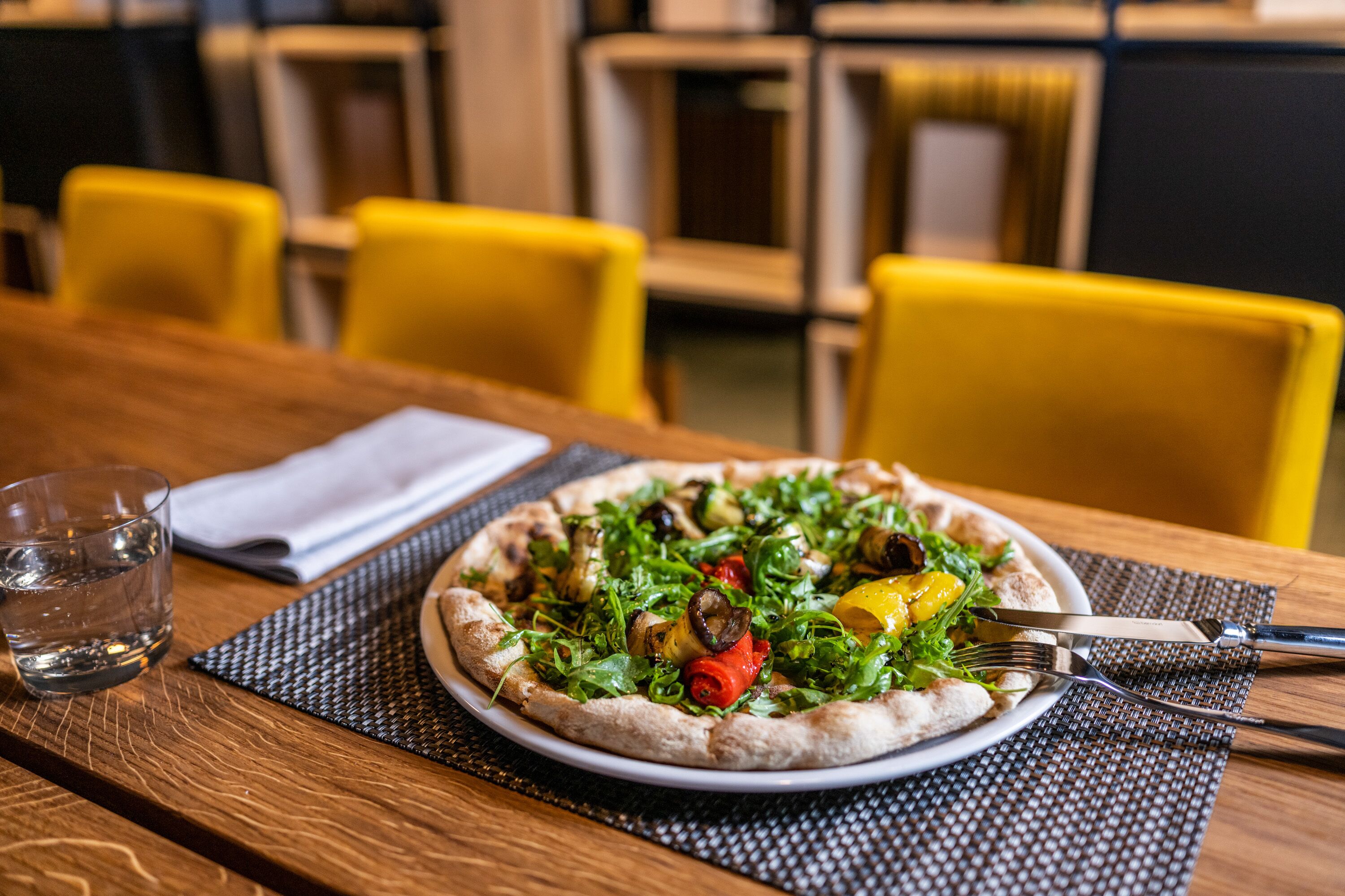 A pizza on a plate with a fork and knife on a table.