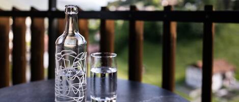 A bottle and a glass on a table with a view of greenery and hills in the background.