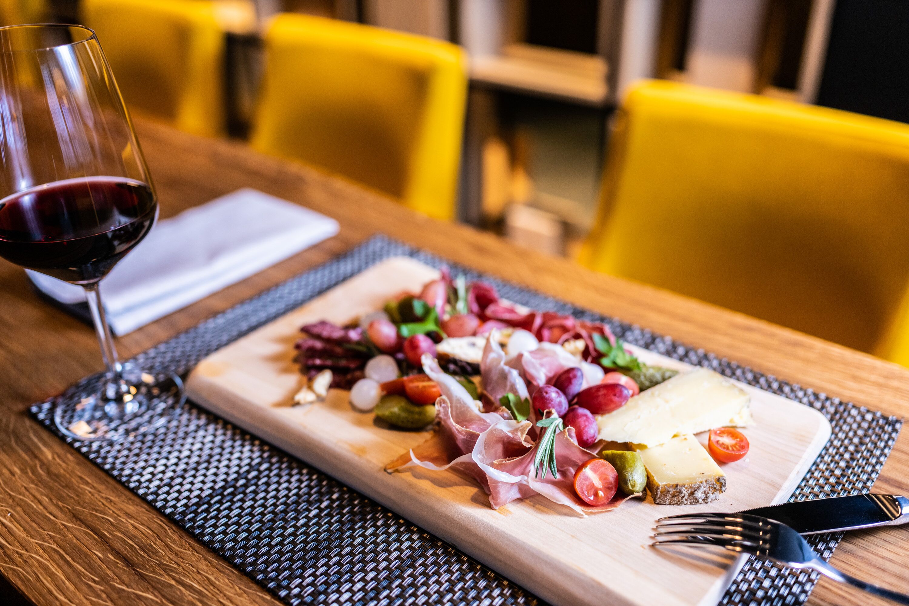 Une table en bois, une planche de charcuterie, un verre de vin rouge et une fourchette.
